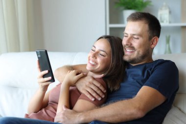 Mutlu çift akıllı telefonlar kullanarak evdeki kanepede oturuyor.