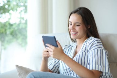 Evdeki kanepede oturup kitap okuyan mutlu kadın.