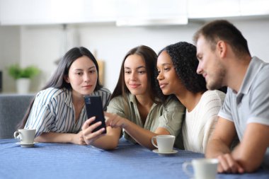 Irklar arası arkadaşlar evdeki bir mutfakta cep telefonu içeriğini kontrol ediyorlar.