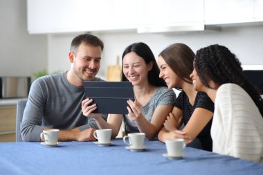 Mutlu ırklar arası arkadaşlar evdeki bir mutfakta tablet kontrol ediyorlar.