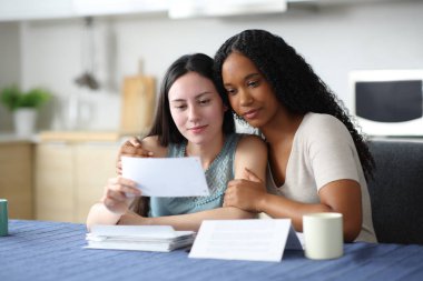 Irklar arası lezbiyen çift evdeki mutfakta hesap özeti okuyorlar.