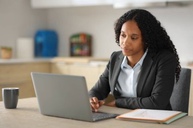 Evdeki mutfakta bilgisayarla çalışan siyahi kadın tele-sekreteri.