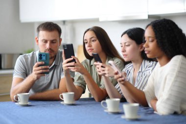 Evdeki mutfakta cep telefonlarını kullanarak birbirlerini görmezden gelen ırklar arası arkadaşlar.