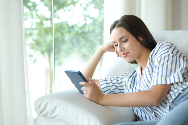Расслабленная женщина читает электронную книгу сидя дома на диване