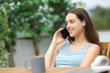 Mutlu kadın telefonda konuşuyor, terasta oturuyor.
