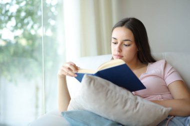 Evdeki kanepede oturup kitap okuyan ciddi bir kadın.