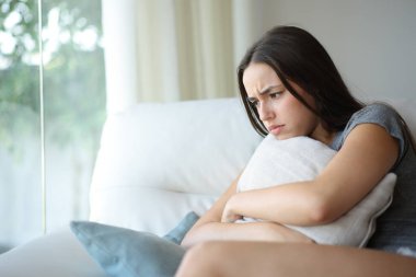 Evdeki kanepede oturan, yastığa sarılmış, sinirli bir kadın.