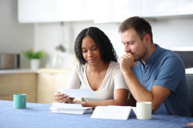 Farklı ırktan çiftler mutfaktaki banka hesap özetini okuyorlar.