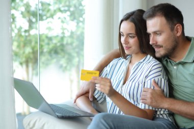 Memnuniyet çift evde bir kanepede oturan kredi kartı ve laptop ile online ödeme