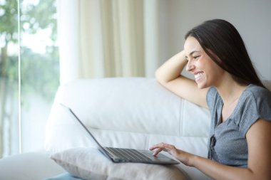Mutlu bir kadın evdeki bir kanepede oturmuş kişisel bilgisayarında internette geziniyor.