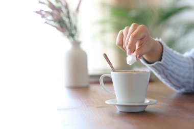 Kahve fincanında şeker küpünü tutan bir kadının elini kapatıyoruz.