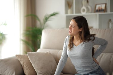 Sırt ağrısı çeken bir kadın evdeki rahat koltukta oturuyor.