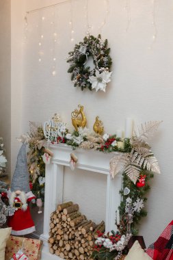 Yapay şömine köknar dalları, mumlar, kırmızı böğürtlenler, altın ren geyiği oyuncakları ile süslenmiş. Odunlar içeride, Noel çelenkleri duvarda.