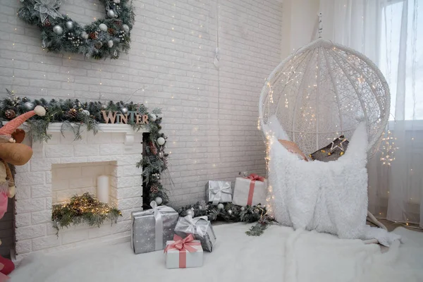 Beautiful white lace cocoon chair with plaid and cushion, golden garland lights in room decorated for Christmas. Magic Christmas vibes