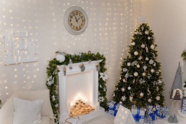 Noel arifesi. Süslü şömine, beyaz ampullü ve çelenkli Noel ağacı. Arka planda yastıklı beyaz kanepe