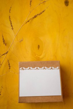 Present box with blank white postcard, branch on bright yellow background, top view, copy space. Birthday, wedding, mothers, Valentines day