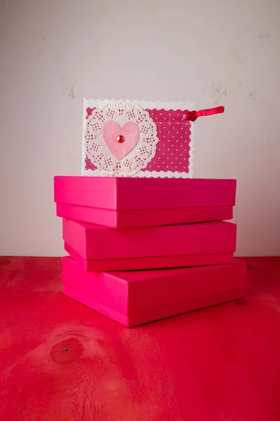 Three bright pink present boxes, postcard with heart on painted wooden background. Happy saint Valentines day. Copy space