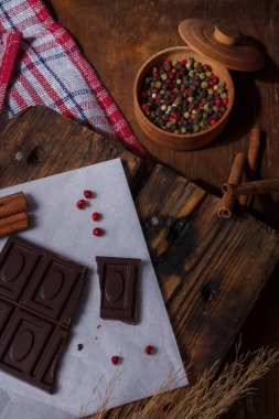 Kırık acı çikolata, acı biber, kırmızı bezelye biberi, tarçın aromalı kağıt, tahta arka plan. Alışılmadık tatlar