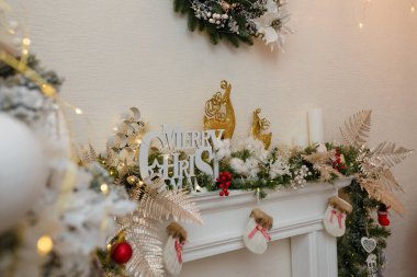 Yapay şömine köknar dalları, mumlar, kırmızı böğürtlenler, altın ren geyiği oyuncakları ile süslenmiş. Mutlu Noel dekoratif unsurları