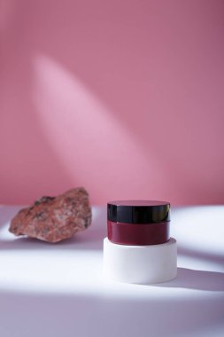 Kahverengi bakım kozmetik kutusu beyaz masada, pembe arka plan sert ışıkta. Model şablon, marka yok, yüz kremi yok, merhem yok.