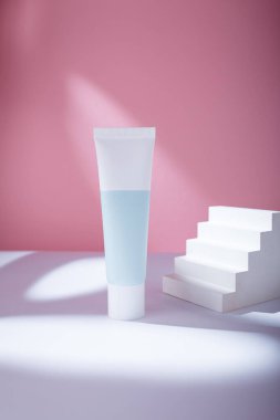 Kozmetik ürünleri pembe arka planda beyaz mavi tüp. Marka modeli yok, boş etiketli şablon. Yüz kremi ya da diş macunu.