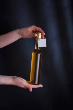 Üzerinde şablon etiketi olan beyaz şarap şişesi tutan eller, markasız. Riesling, chardonnay, sauvignon blanc. Siyah arkaplanda alkol içeceği