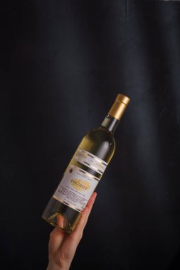 İzmail, Ukrayna. Kasım 2022. Besarabian şaraphanesi. El ele tutuşan beyaz şarap şişesi Riesling. Siyah arkaplanda alkol içeceği