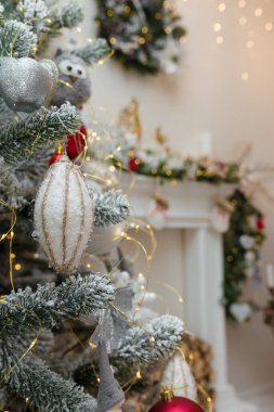 Noel ağacı yapay kar ve dekore edilmiş şömine arka planında ampullerle kaplı. Mutlu yıllar için ağaç dalları ve oyuncaklar
