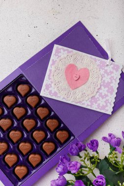 İzmail, Ukrayna. 14 Şubat 2022. Mor kalp şeklinde çikolata Milka, çiçekler, beyaz üzerine kartpostal. Sevgililer Günü tatlıları