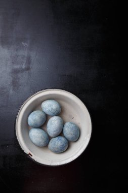 Paskalya yumurtaları siyah ahşap arka planda beyaz kâseye maviye boyanmış. Üst görünüm, kopyalama alanı, dikey çekim