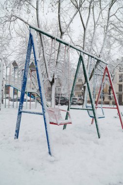Parlak renkli çocukların oyun parkı karlı arka planda karla kaplı. Kar yağışı yağışı, tipi ya da kar fırtınası
