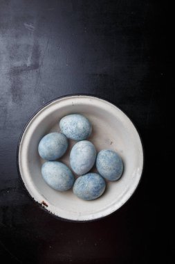 Paskalya yumurtaları siyah ahşap arka planda beyaz kâseye maviye boyanmış. Üst görünüm, kopyalama alanı, dikey çekim