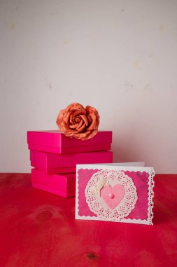 Three bright pink present boxes, fabric rose flower, postcard with heart on painted wooden background. Happy saint Valentines day. Copy space