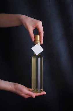 Üzerinde şablon etiketi olan beyaz şarap şişesi tutan eller, markasız. Riesling, chardonnay, sauvignon blanc. Siyah arkaplanda alkol içeceği