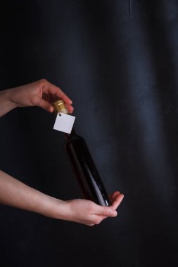 Kadın elleri 250 ml kırmızı şarap tutuyor. Etiketi sahte, siyah arka planda markası yok. Alkol içeceği, kopyalama alanı