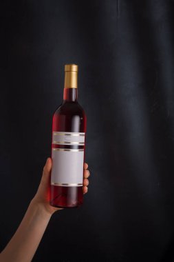 Elinde sahte etiketli pembe şarap şişesi, siyah arka planda markası yok. pinot noir. Alkol içeceği, kopyalama alanı