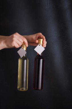 250 ml 'lik iki beyaz ve kırmızı şarap şişesini elinde tutan bir kadın el. Siyah arka planda hiçbir marka taklit edilmemiş. Dikey çekim, boşluğu kopyala