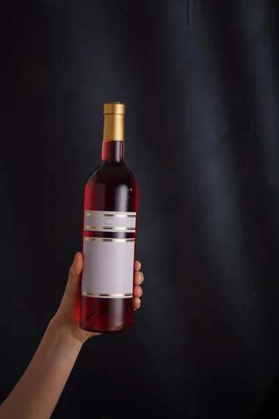 hand holding bottle of pink wine with mock up label, no brand on black background. pinot noir. Alcohol drink, copy space