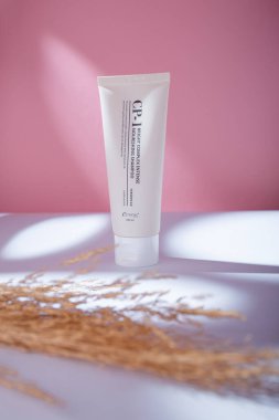 Izmail, Ukraine. May 2022. Esthetic bright complex intense nourishing hair shampoo on pink background, reeds branch in harsh shadows