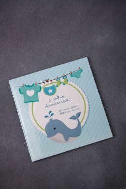 Izmail, Ukraine. June 2020. Baby photo album or photobook with blue whale on grey background. Inscription: Artem 1 year, 12 June, some data
