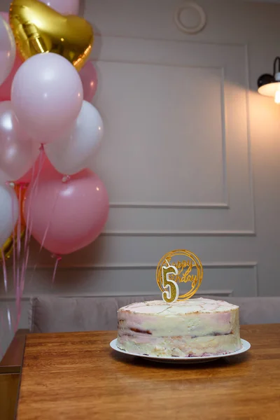Happy Birthday cake with number 5 shaped candle on brown table, pink white balloons. Festive cake for five years old child anniversary