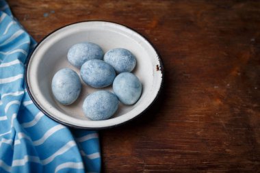 Beyaz kasede mavi renkli paskalya yumurtaları, kahverengi ahşap kırsal masa arka planında mavi çizgili kumaş. Boşluğu kopyala