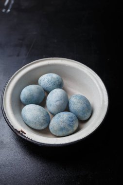 Easter eggs painted blue in white bowl on black wooden background. Copy space, vertical shot