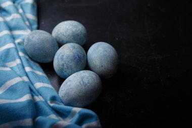 Paskalya yumurtaları siyah ahşap arka planda beyaz kaseye çizgili kumaşla maviye boyanmış. Yakın çekim, boşluğu kopyala