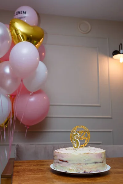 Happy Birthday cake with number 5 shaped candle on brown table, pink white balloons. Festive cake for five years old child anniversary
