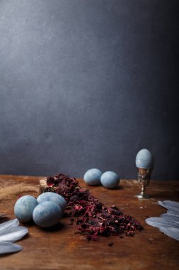 DIY mavi boyalı Paskalya yumurtaları, yumurta kabında bir yumurta, kuru Hibiscus çayı ve ahşap arka planda gümüş dekoratif tüyler, kopya alanı, dikey çekim alanı