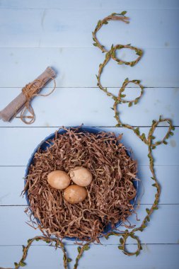 Plate decorated as bird nest with brown colored eggs on blue background. Happy Easter. Top view, copy space, vertical shot