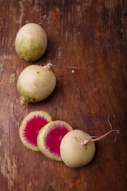 Whole and sliced fresh watermelon radish, daikon root vegetables with white skin and purple inside on brown wooden background