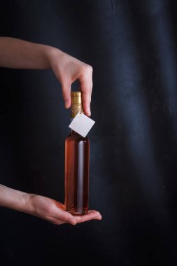 Kadın eli 250 ml 'lik pembe şarap tutuyor. Etiketi taklit edilmiş, siyah arka planda markası yok. Alkol içeceği, kopyalama alanı