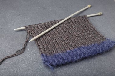 Gri arkaplanda örgü örgüsü ve akrilik iplik kumaşı parçaları olan örgü iğneleri..
